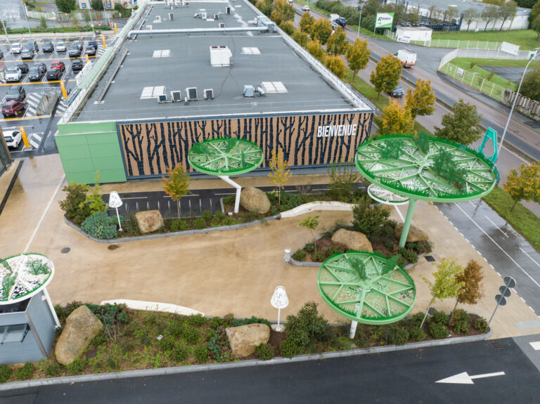 Situé à Pontault-Combault, ce centre commercial se veut moderne et écologique. Le bardage en stratifié haute pression sublime l'identité du site, avec une finition immitation bois et un découpage en forme de troncs d'arbres. Les parasols, eux aussi, rappellent la nature avec les découpes laser en forme de feuille. Un travail de précision pour un rendu de qualité.