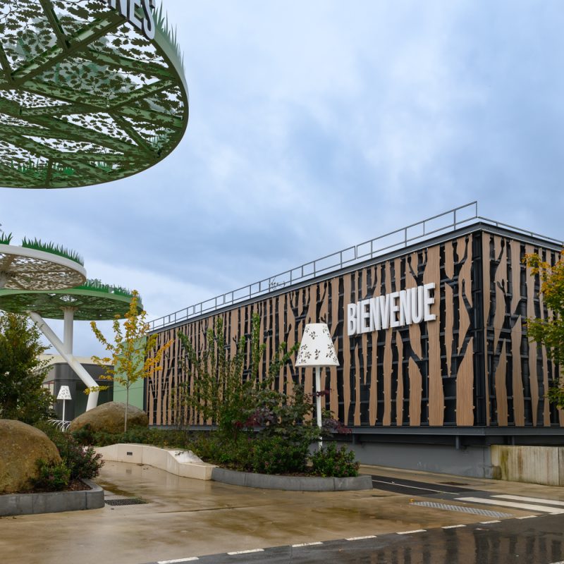 Situé à Pontault-Combault, ce centre commercial se veut moderne et écologique. Le bardage en stratifié haute pression sublime l'identité du site, avec une finition immitation bois et un découpage en forme de troncs d'arbres. Les parasols, eux aussi, rappellent la nature avec les découpes laser en forme de feuille. Un travail de précision pour un rendu de qualité.