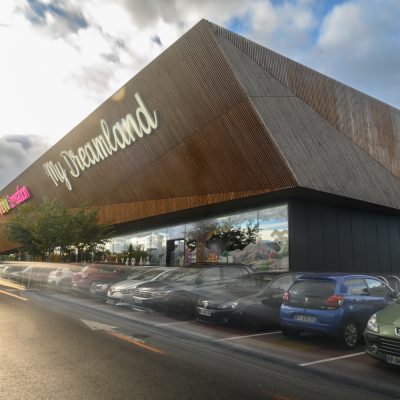 À Osny, ce centre commercial multi-enseignes est un centre de shopping, restauration et de loisirs. Parties vitrées, bardage en bois et en acier sont les éléments qui composent son habillage, montrant l'univers du possible, nottament avec le bardage en bois aux formes irrégulières.