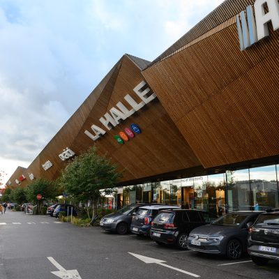 À Osny, ce centre commercial multi-enseignes est un centre de shopping, restauration et de loisirs. Parties vitrées, bardage en bois et en acier sont les éléments qui composent son habillage, montrant l'univers du possible, nottament avec le bardage en bois aux formes irrégulières.