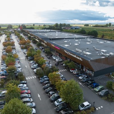 À Osny, ce centre commercial multi-enseignes est un centre de shopping, restauration et de loisirs. Parties vitrées, bardage en bois et en acier sont les éléments qui composent son habillage, montrant l'univers du possible, nottament avec le bardage en bois aux formes irrégulières.